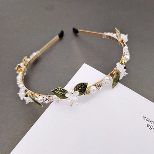 Detail of floral headband with white enamel flowers, green leaves, and white pearls