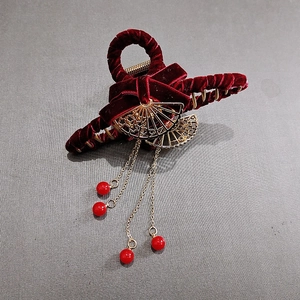 Dettaglio del fermaglio per capelli in velluto rosso con nappe dorate e decori a ventaglio