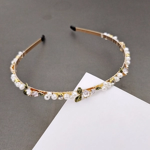 Close-up of golden metal headband with white pearls, pink flowers and green enamel leaves