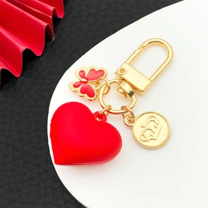 Red 3D resin heart keychain with golden butterfly and crown charms on leather background