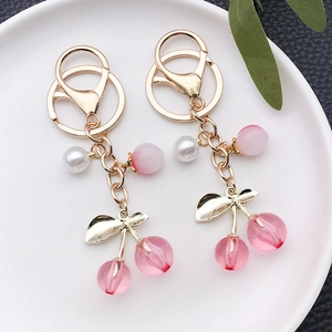 Pink translucent cherry keychain with pearls and gold leaf accents on a white plate