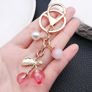 Pink translucent cherry keychain with pearls and golden leaf held against a white rock