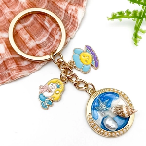 Close-up of golden mermaid keychain with starfish, blue shell pendant and white pearl detail