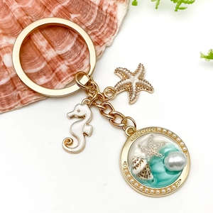 Détails des breloques hippocampe, étoile de mer et perle sur un pendentif porte-clés doré