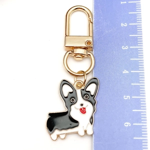 Close-up of a black and white enamel Corgi keychain with a gold metal ring and ruler for scale