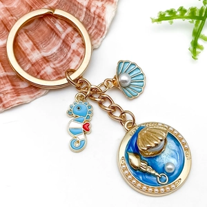Détail d'un porte-clés marin doré avec hippocampe en émail bleu, coquillage et perles