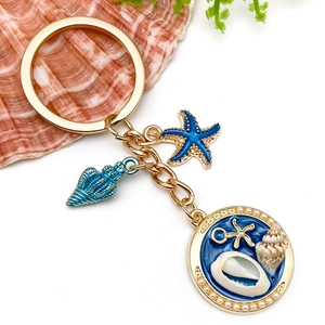 Vue détaillée du porte-clés doré avec pendentifs étoile de mer et coquillage en émail bleu