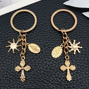Set of two gold sun flame cross alloy keychains on a premium black leather texture