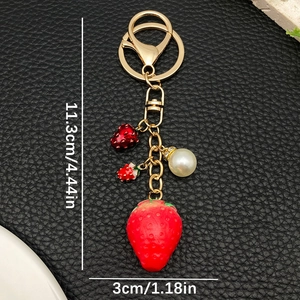 Detailed view of red resin strawberry keychain with white pearl and gold hardware