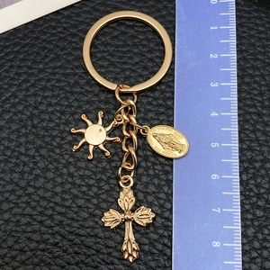 Golden sun and cross keychain with religious medal on black leather background