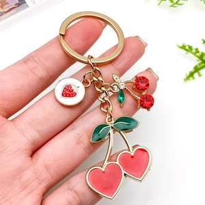 Llavero de cereza y fresa dorado con pedrería roja y colgantes de esmalte de corazón