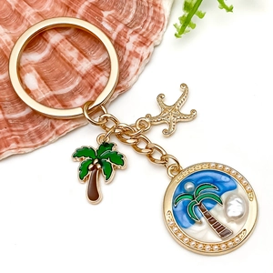 Détail d'un porte-clés tropical doré avec palmier et breloque en émail océan