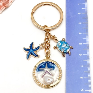 Detail of blue turtle and starfish charms on gold keychain with sea wave pendant