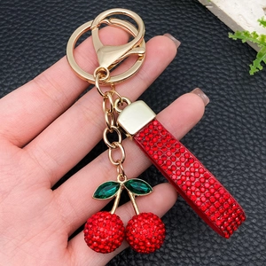 Sparkling red cherry keychain with green leaves and gold lobster clasp on black background