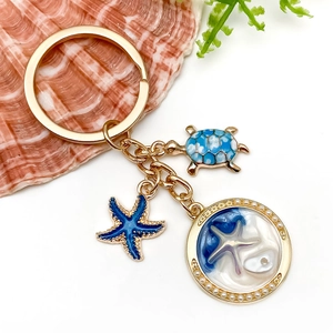 Close-up of ocean-themed blue turtle and starfish charms with shell inlay on a golden keychain