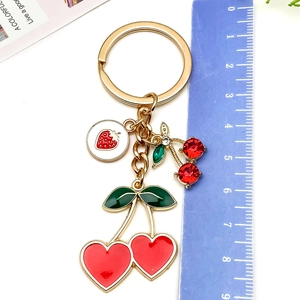 Vista macro de llavero de cereza de 9 cm con corazones rojos y detalles en metal dorado