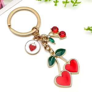 Detalle de llavero dorado con cerezas rojas de corazón y colgante de fresa con pedrería
