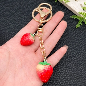 Realistic red resin strawberry keychain with gold leaves and lobster clasp on black background