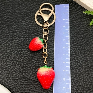 Detailed view of red resin strawberry charms with gold keychain on black leather