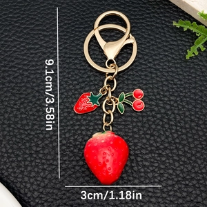 Resin strawberry and cherry keychain with golden hardware on a black background