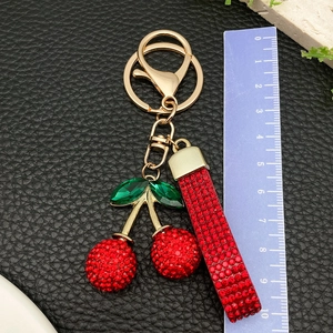 Macro view of a red rhinestone cherry keychain with green crystal leaves on black leather