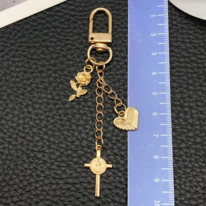 Porte-clés rose dorée avec ailes d'ange et pendentif croix mesuré par une règle