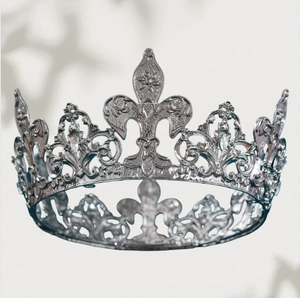 Close-up of a silver vintage tiara featuring fleur-de-lis and intricate filigree patterns