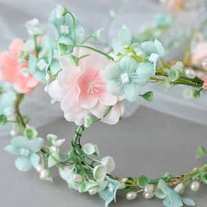 Détail d'un bandeau bohème avec des fleurs de soie roses, des perles blanches et tiges