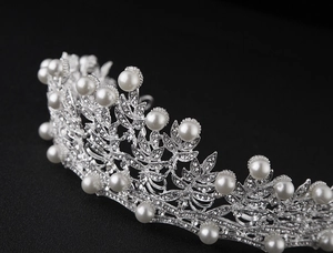 Detailed view of silver bridal crown featuring pearls and rhinestones on black background