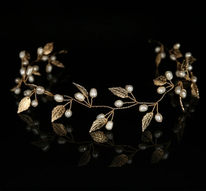 Detail of bridal headband with gold leaves and white pearls on reflective black background
