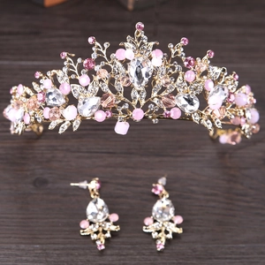 Detalle de corona dorada y pendientes de gota con cristales rosas sobre madera