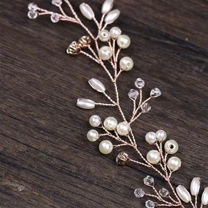 Dettaglio dell'acconciatura da sposa oro rosa con perle e cristalli su legno scuro