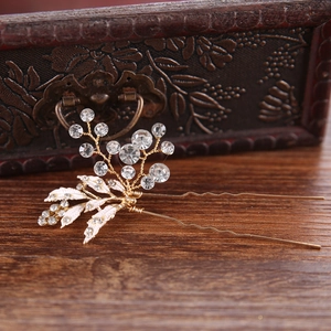 Close-up of golden bridal hair comb with white enamel leaves and crystal rhinestones