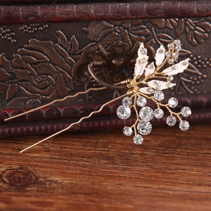 Macro view of gold bridal hair comb with white enamel leaves and shimmering rhinestones