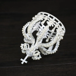 Elegant silver crown with pearls and cross detail on a dark wooden background