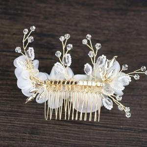 Elegant bridal hair comb with white chiffon flowers and gold leaf beads on wood surface