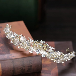Close-up of golden bridal crown with white enamel leaves and crystal rhinestones on books