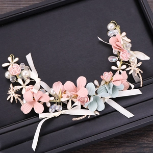 Détail de coiffe florale avec fleurs en tissu rose, perles blanches et rubans pendants