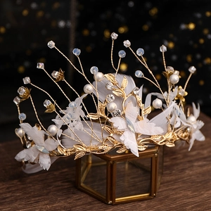 Exquisite bridal crown with pearls and feathers displayed on a golden glass case