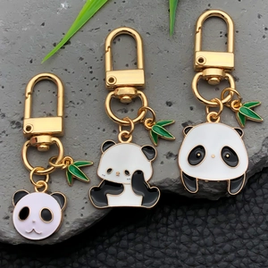 Three cute cartoon panda metal keychains with bamboo leaves on a natural stone background
