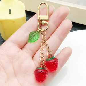 Creative resin strawberry keychain with green leaf and golden D-ring clasp held by hand