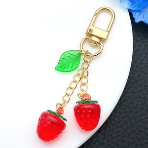 Close-up of dual red resin strawberries with green leaf and golden lobster clasp