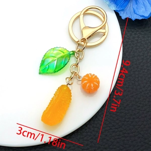 Creative resin orange keychain with green leaves and gold ring on a white tray