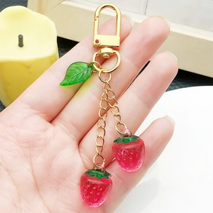 Cute resin strawberry keychain with green leaf and golden clasp held in hand