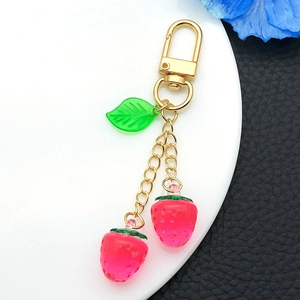Detail of red resin strawberries with green leaves and golden metal keychain on a white plate