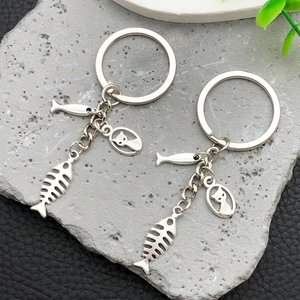 Detail shot of silver metal cat and fish bone charms on keychains over a stone surface