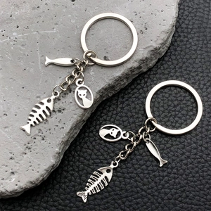 Detail of silver cat and fish bone charms on metal keychains over textured leather