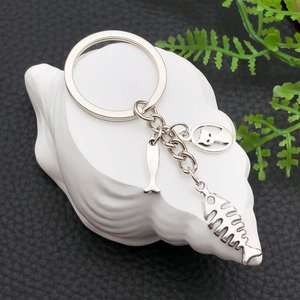 Antique silver cat and fish bone metal keychain displayed on white shell stand