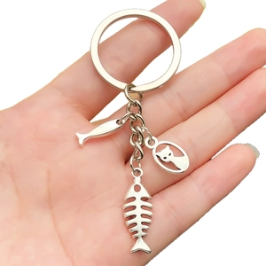 Silver antique style cat and fish charms keychain held in hand on white background