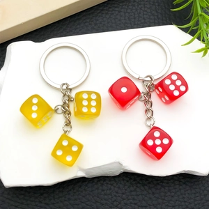 Detail of red and yellow resin dice keychains on a textured stone and leather surface